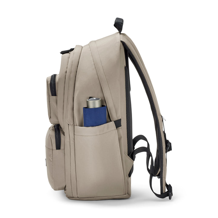 Beiger Rucksack No 3 Advanced mit zwei Außentaschen und seitlicher blauer Tasche mit Zeitung und silberner Trinkflasche