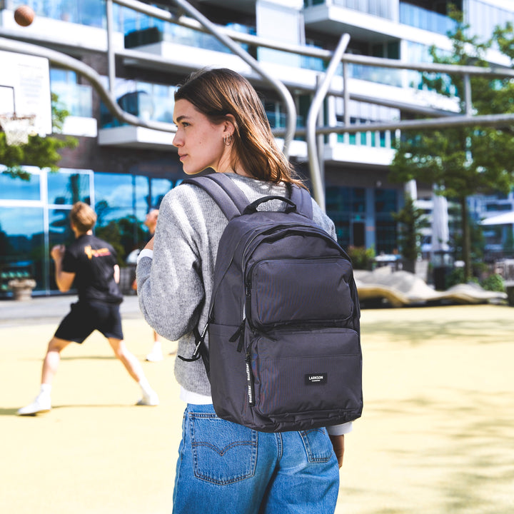 Jugendliche trägt schwarzen Rucksack 'Rucksack No 3 Advanced' von Larkson, trägt grauen Pullover und blaue Jeans
