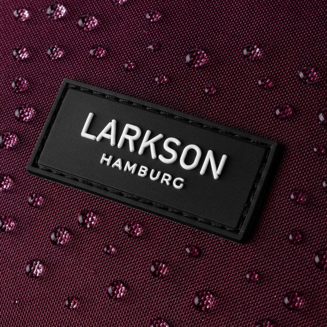 Nahaufnahme des LARKSON Hamburg Logos auf einem wasserabweisenden, dunkellila Rucksack mit Wassertropfen