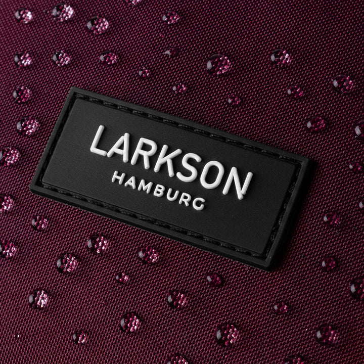Nahaufnahme des LARKSON Hamburg Logos auf einem wasserabweisenden, dunkellila Rucksack mit Wassertropfen