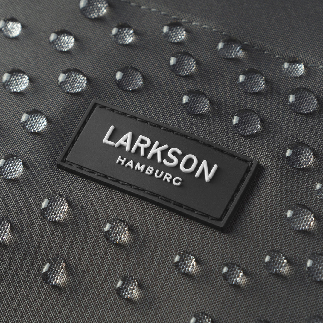 Nahaufnahme des schwarzen LARKSON Hamburg Logos auf wasserdichtem Rucksackstoff mit Wassertropfen