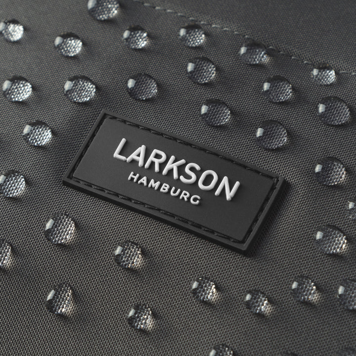 Nahaufnahme des schwarzen LARKSON Hamburg Logos auf wasserdichtem Rucksackstoff mit Wassertropfen