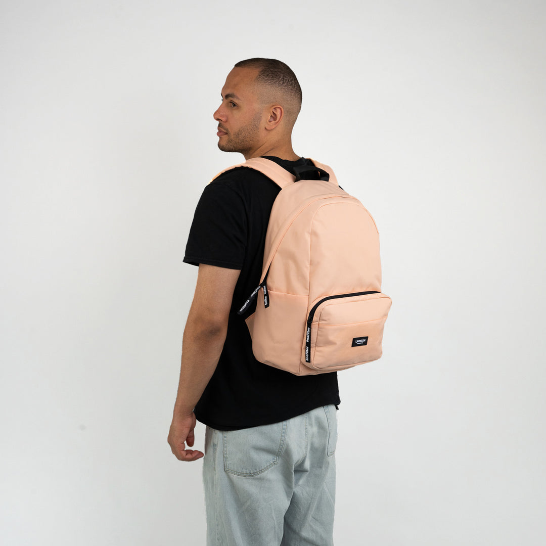 Mann mit hellem Pfirsichfarbener LARKSON Rucksack No 3, schwarzes T-Shirt, hellblaue Jeans