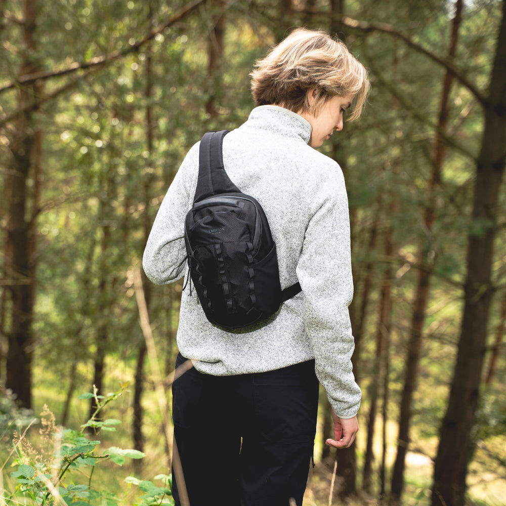 Frau steht in der Natur und trägt die schwarze Sling Bag von Larkson.