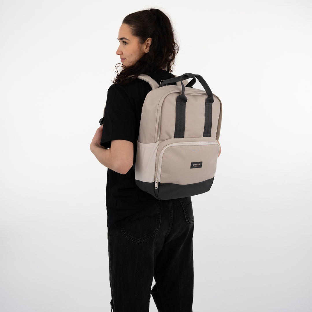 Frau trägt beige-grauen Rucksack 'Rucksack No 6' von LARKSON, kombiniert mit schwarzem T-Shirt und Hose