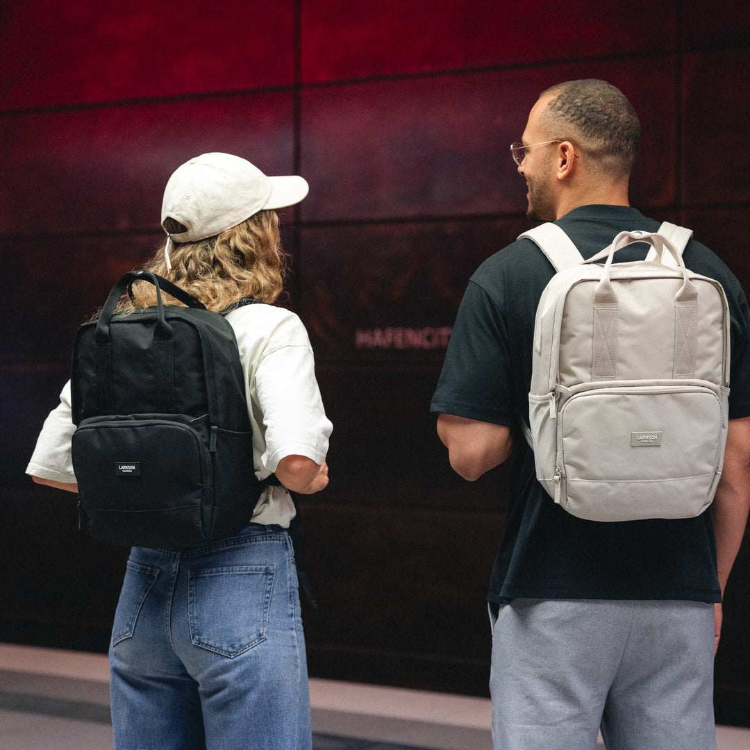 Zwei Personen tragen LARKSON Rucksack No 6, eine schwarz, die andere beige, in urbaner Umgebung