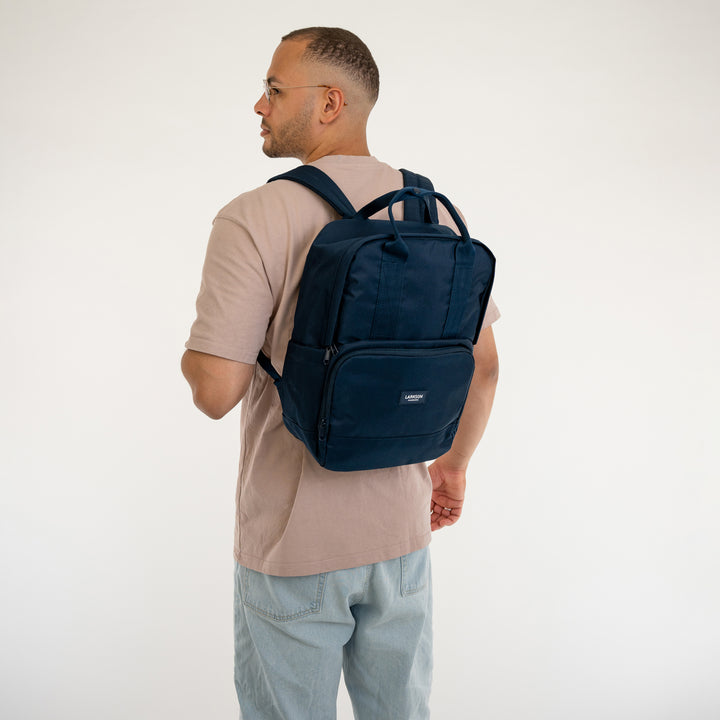 Mann mit beige T-Shirt und hellen Jeans trägt dunkelblauen Rucksack No 6 von LARKSON
