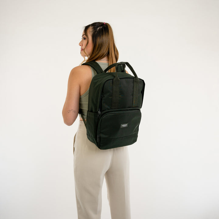 Frau trägt LARKSON Rucksack No 6 in modernem dunklem Grün, schlank, mit zwei Griffen und Fronttasche