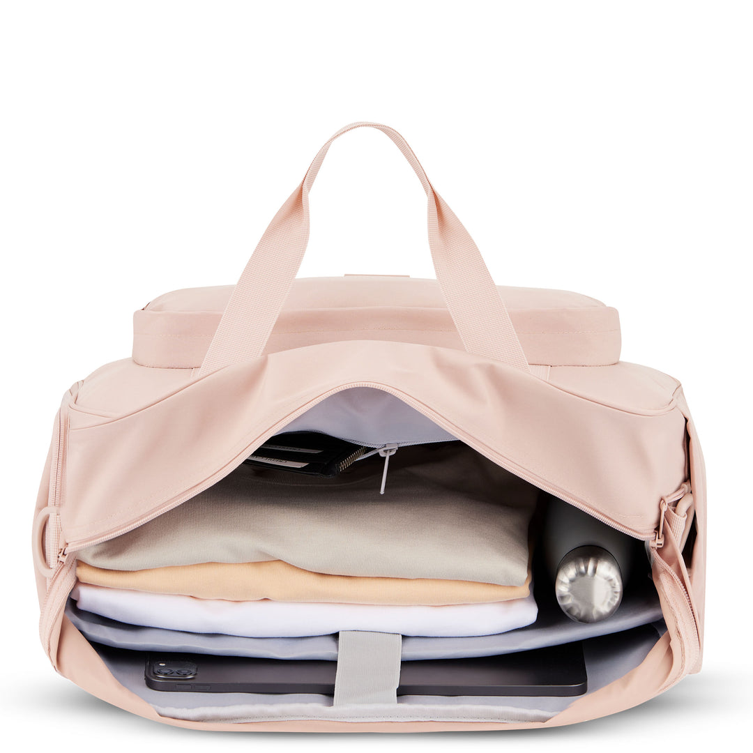 Rosa Reisetasche Finja geöffnet mit Kleidungsstücken, Wasserflasche und technischen Geräten