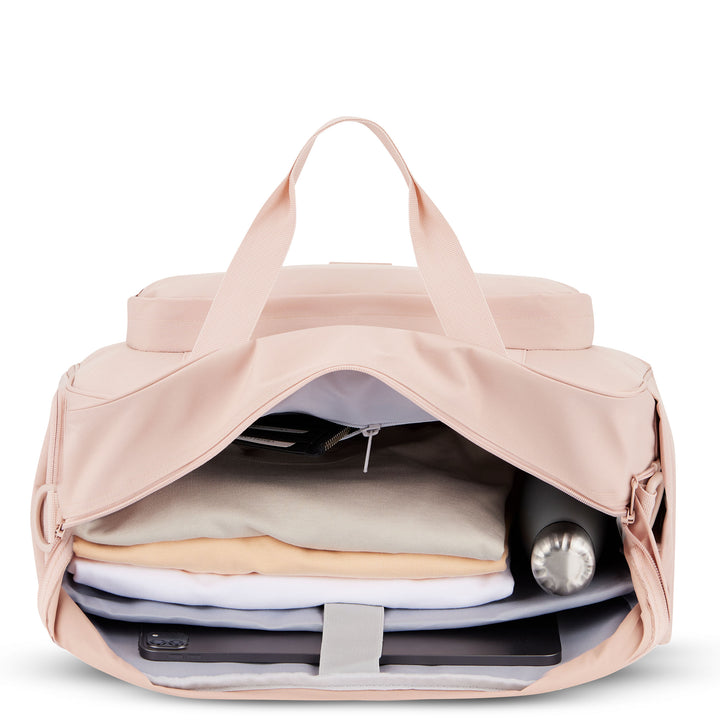 Rosa Reisetasche Finja geöffnet mit Kleidungsstücken, Wasserflasche und technischen Geräten