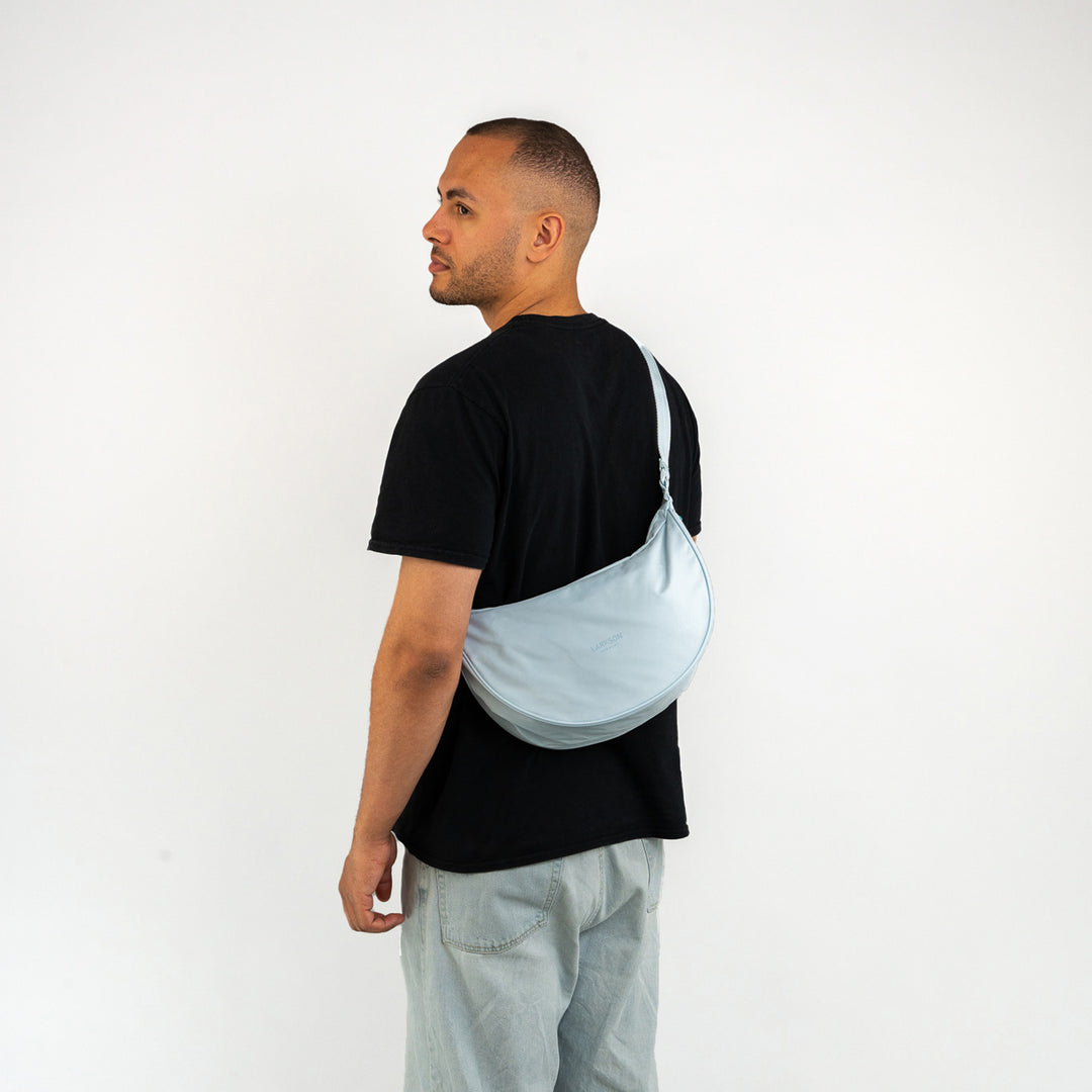 Mann mit schwarzem T-Shirt trägt halbrunde blaue Half Moon Bag Solveig Medium von LARKSON über der Schulter
