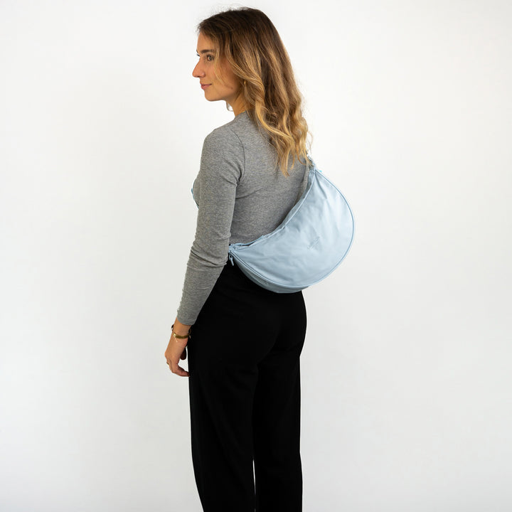 Frau mit halbmondförmiger blauer Half Moon Bag Solveig Medium über der Schulter