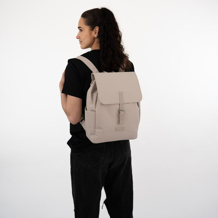 Damen mit beigem Rucksack Ida von LARKSON, seitlich stehend, schwarzes Oberteil und Hose