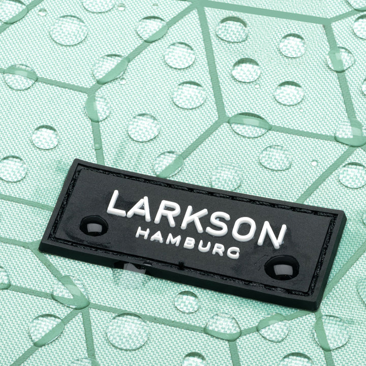Nahaufnahme des schwarzen LARKSON Hamburg Labels auf mintgrünem, wasserabweisendem Rucksackmaterial mit Wassertropfen