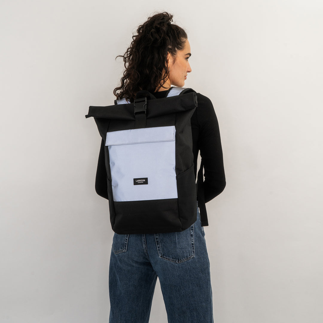 Frau trägt schwarzen und reflektierenden Rolltop Rucksack No 4 von LARKSON mit großer Fronttasche