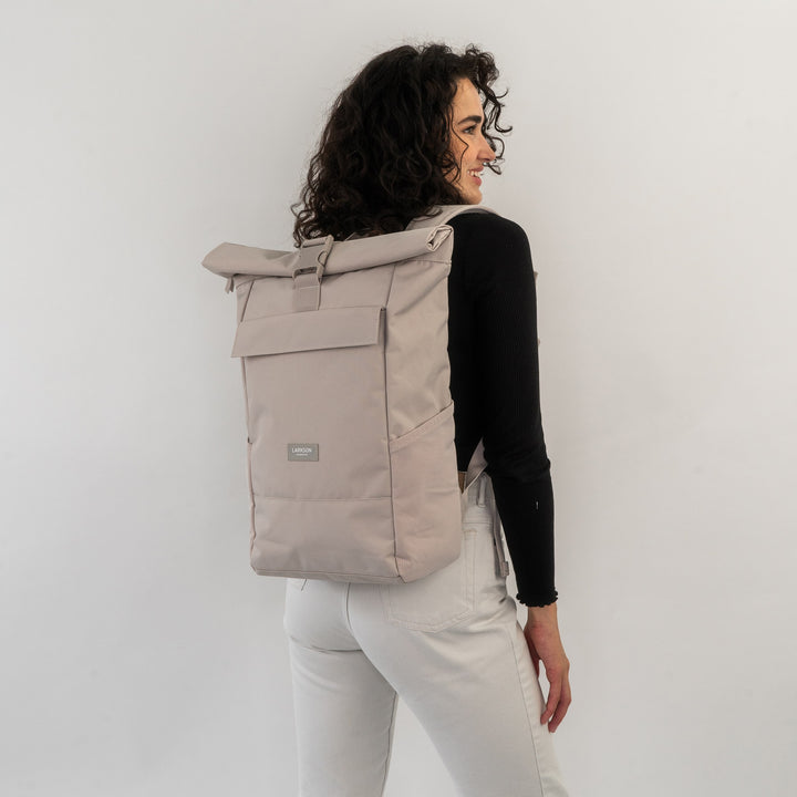 Frau mit lockigen Haaren trägt beige Rolltop Rucksack No 4 von Larkson, schwarzer Pullover, helle Hose