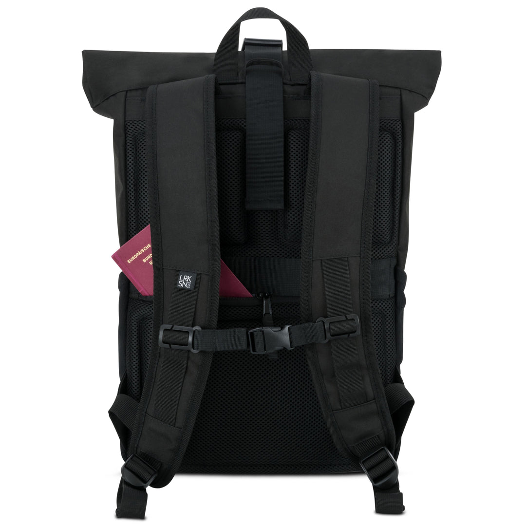 Rückseite des schwarzen Rolltop Rucksacks No 4 mit gepolsterten, verstellbaren Trägern und einem burgunderfarbenen Reisepass in der Seitentasche