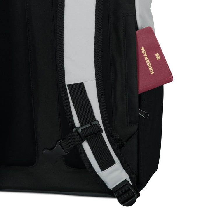 Schwarzer Rolltop Rucksack No 2 mit weiß gepolstertem Schultergurt und einem roten Reisepass in der Seitentasche