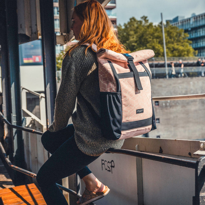 Frau trägt einen rosa Rolltop Rucksack No 2 von LARKSON mit schwarzem Rand, draußen sitzend