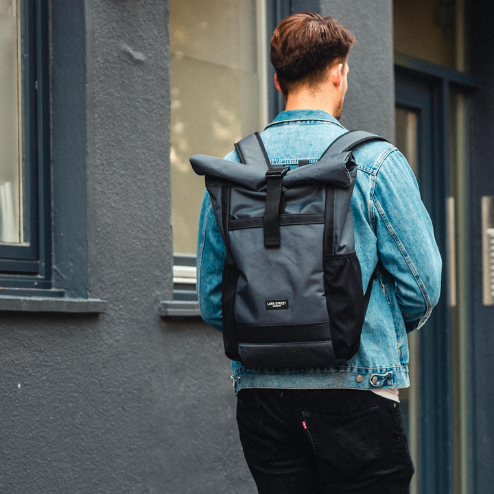 Mann mit hellblauer Jeansjacke trägt anthrazitfarbenen Rolltop Rucksack No 2 von LARKSON