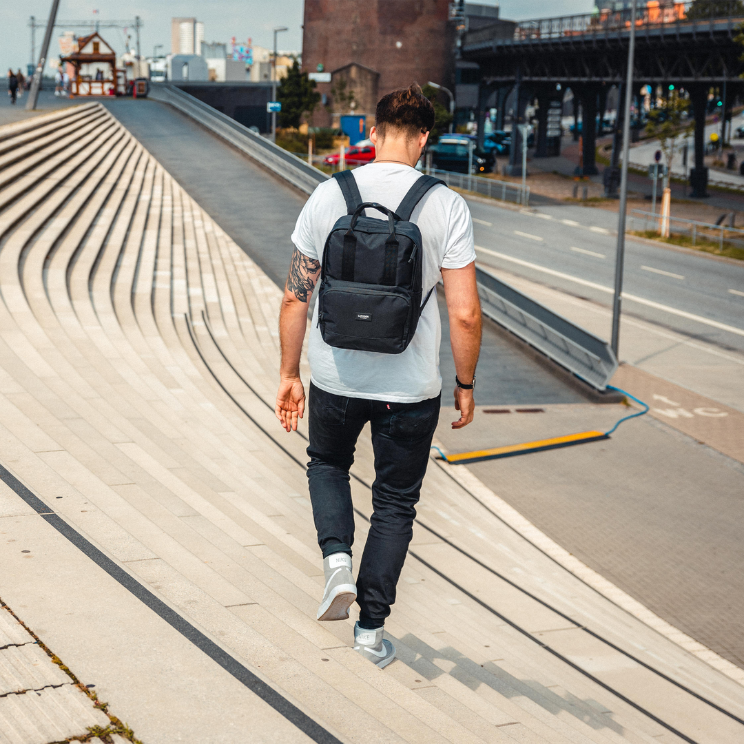 Mann trägt schwarzen Rucksack No 6 von LARKSON, schreitet eine Treppe hinunter in urbaner Umgebung