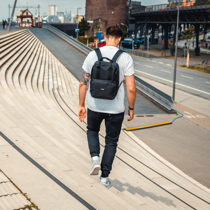 Mann trägt schwarzen Rucksack No 6 von LARKSON, schreitet eine Treppe hinunter in urbaner Umgebung