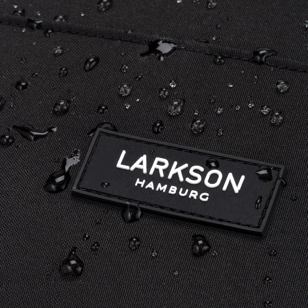 Nahaufnahme des Larkson Hamburg Logos auf schwarzem, wasserdichtem Rucksackstoff mit Wassertröpfchen