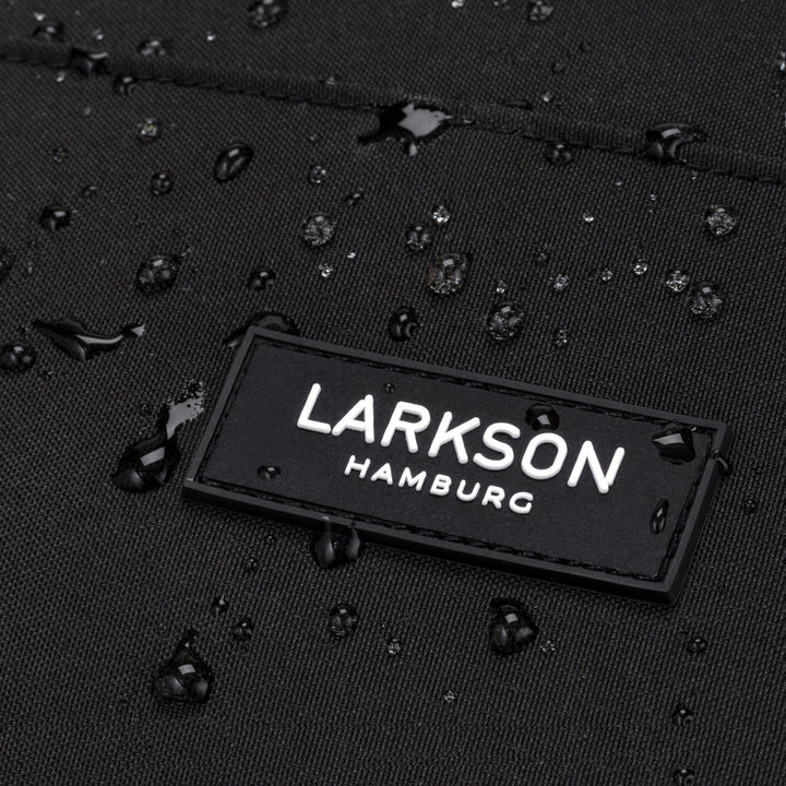 Nahaufnahme des Larkson Hamburg Logos auf schwarzem, wasserdichtem Rucksackstoff mit Wassertröpfchen