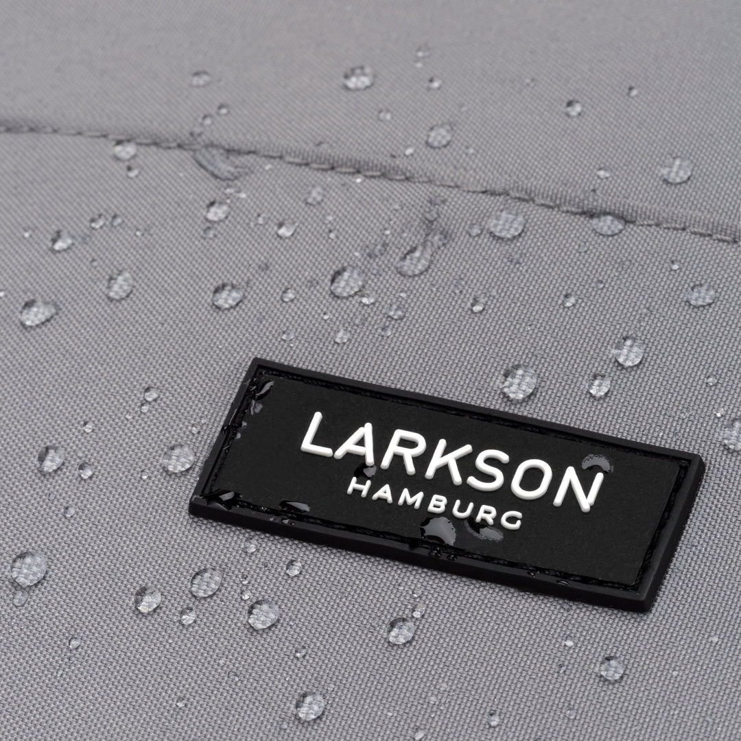 Nahaufnahme des schwarzen LARKSON Hamburg Logos auf grauem wasserdichtem Rucksackmaterial mit Wassertropfen