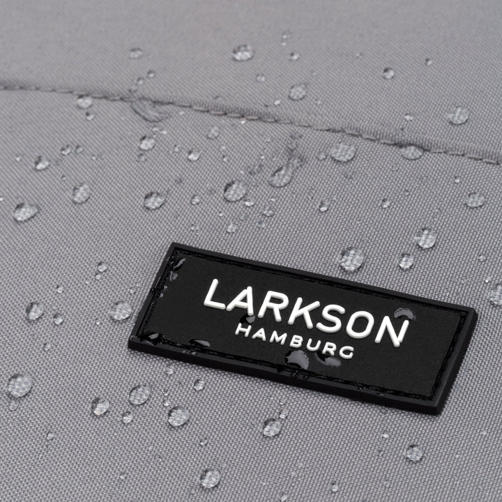 Nahaufnahme des schwarzen LARKSON Hamburg Logos auf grauem wasserdichtem Rucksackmaterial mit Wassertropfen
