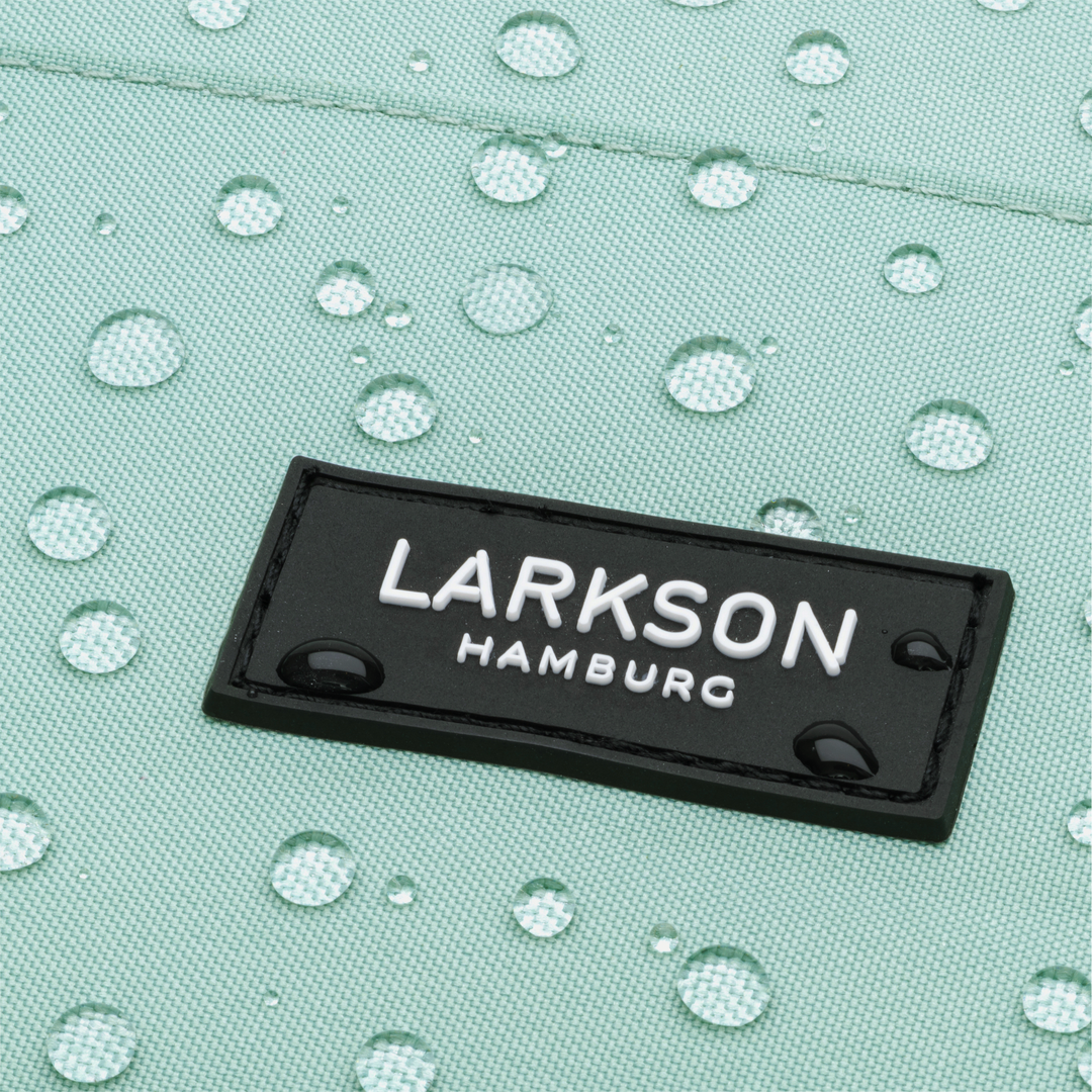 Nahaufnahme des schwarzen LARKSON Hamburg Logos auf mintgrünem, wasserdichtem Rucksackmaterial mit Wassertropfen