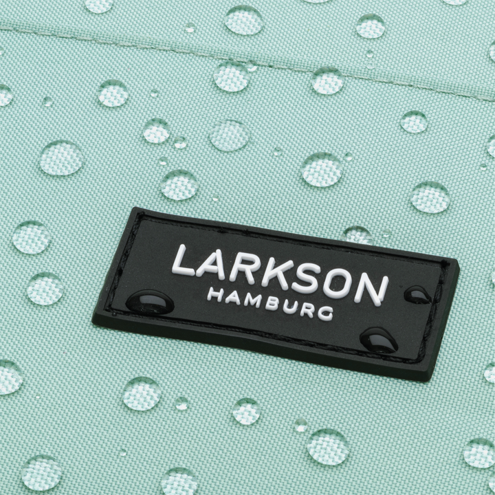 Nahaufnahme des schwarzen LARKSON Hamburg Logos auf mintgrünem, wasserdichtem Rucksackmaterial mit Wassertropfen