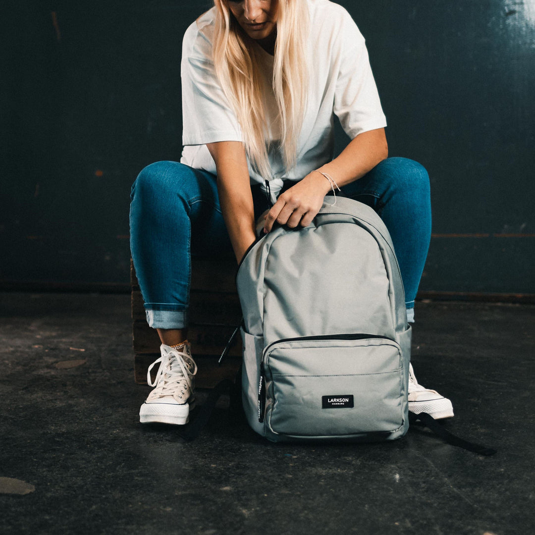 Teenager-Mädchen mit hellgrauem LARKSON Schulrucksack No 3 sitzt in Sportkleidung