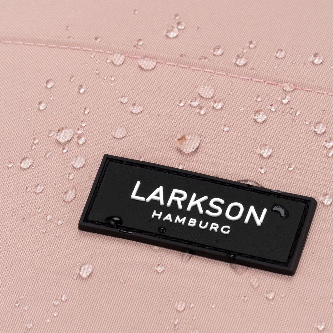 Nahaufnahme eines rosafarbenen Rucksacks mit dem schwarzen LARKSON Hamburg Logo und Wassertröpfchen auf der Oberfläche