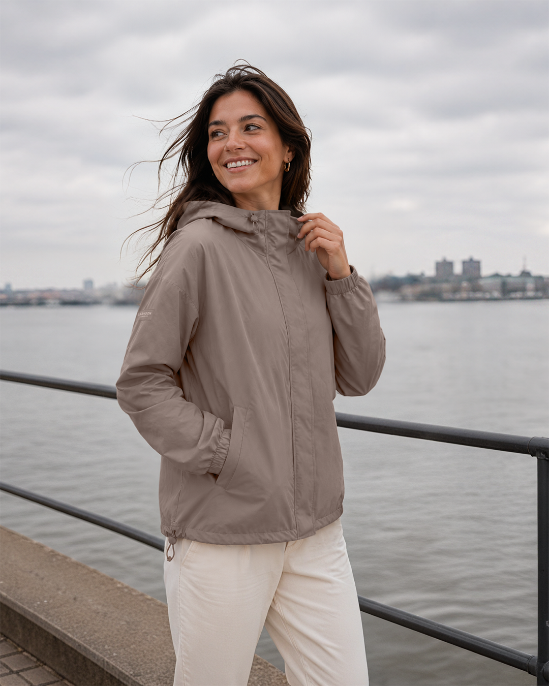 Frau steht am Wasser und trägt Larkson Regenjacke Elin in taupe | KI generiertes Bild
