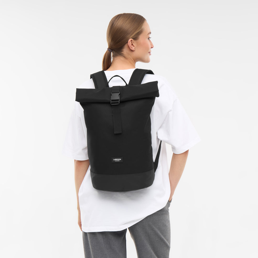 Schwarzer Rolltop Rucksack Janne Small von LARKSON an einer Frau mit weißem T-Shirt und grauer Hose