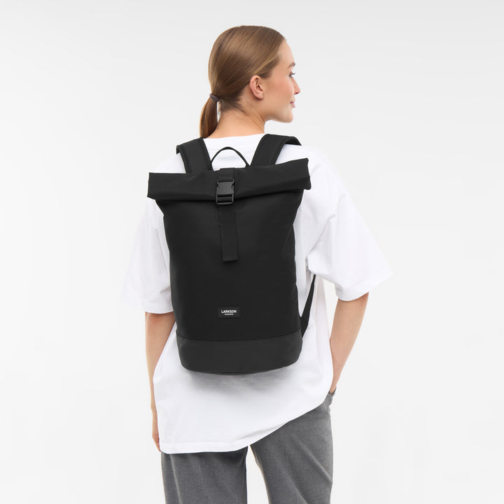 Schwarzer Rolltop Rucksack Janne Small von LARKSON an einer Frau mit weißem T-Shirt und grauer Hose