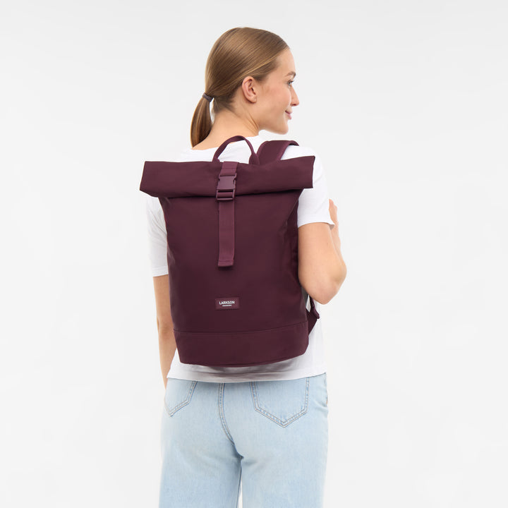 Frau mit hellem T-Shirt und Jeans trägt dunkellila Rolltop Rucksack Janne Small von LARKSON