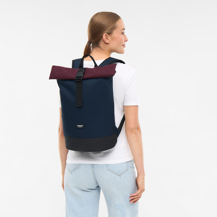 Rolltop Rucksack Janne Small von Larkson in Blau mit burgunderfarbenem Rollverschluss auf Rücken einer Frau