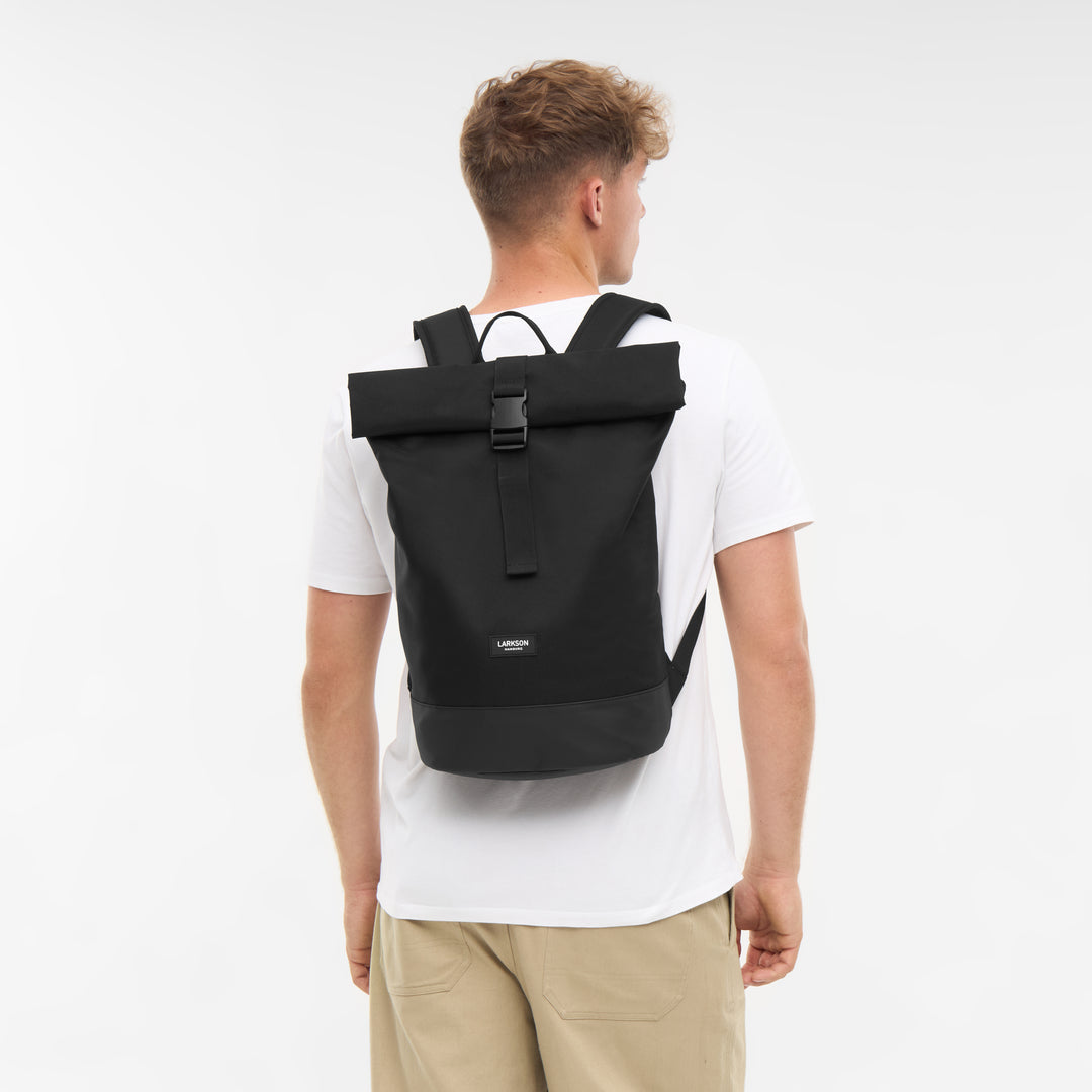 Junger Mann trägt schwarzen LARKSON Rolltop Rucksack Janne Small mit Schnallenverschluss