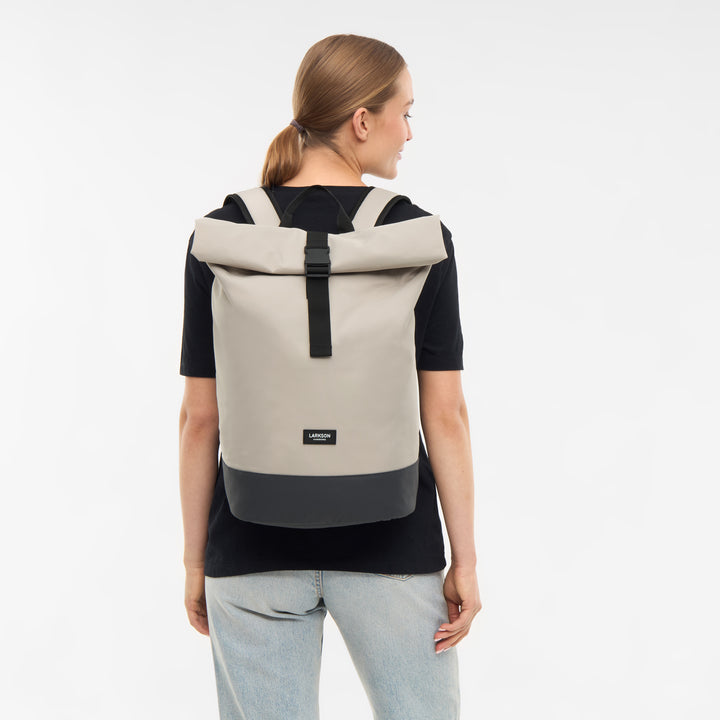 Frau trägt hellbeigen Rolltop Rucksack 'Janne' von LARKSON mit schwarzem Boden und Riemen