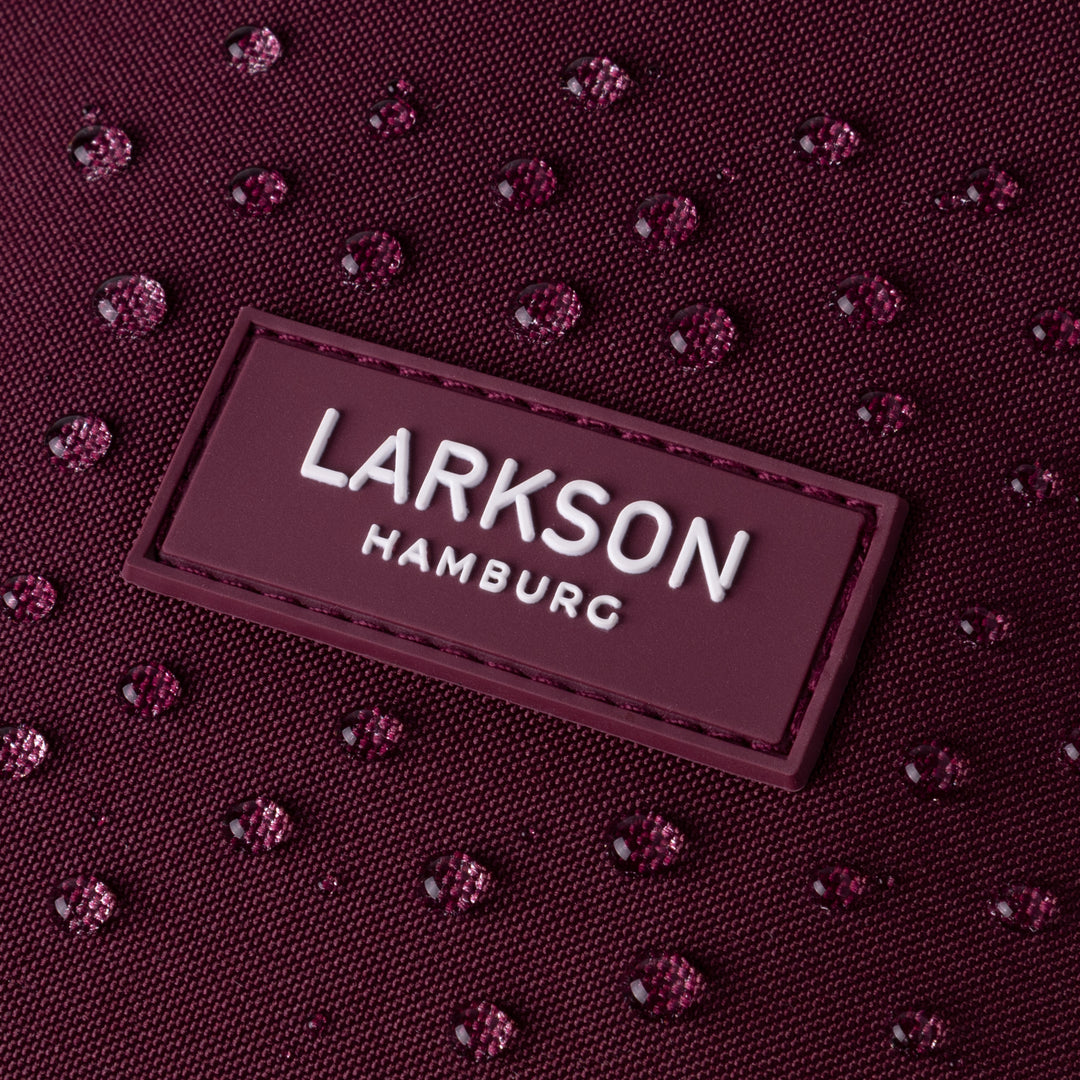 Nahaufnahme des wasserabweisenden burgunderroten Rolltop Rucksack Janne Small von Larkson mit Logo und Wassertropfen