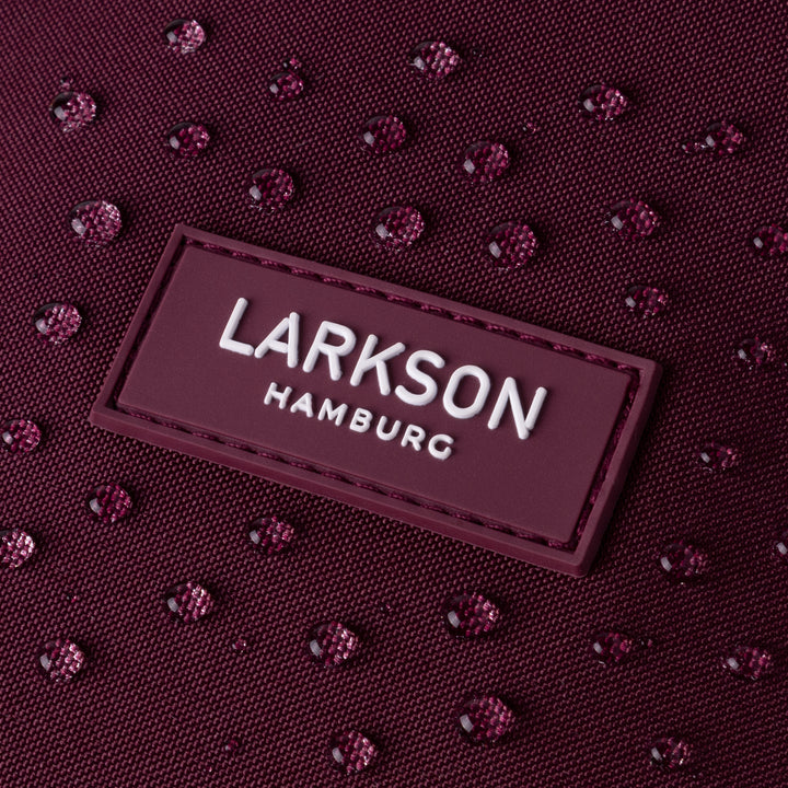Nahaufnahme des wasserabweisenden burgunderroten Rolltop Rucksack Janne Small von Larkson mit Logo und Wassertropfen
