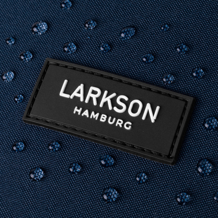 Nahaufnahme des 'LARKSON HAMBURG' Logos auf wasserabweisendem blauem Stoff mit Wassertropfen